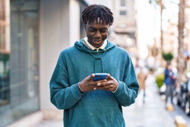 Sokakta akıllı telefon kullanan, kendinden emin gülümseyen Afrikalı Amerikalı bir adam.