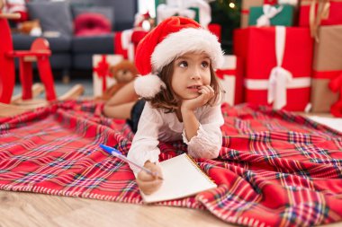 Sevimli İspanyol kız Noel Baba mektubu yazıyor. Evdeki Noel ağacının yanında yerde yatıyor.