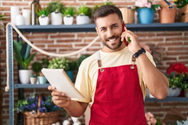 Young hispanic man florist talking on smartphone reading book at florist