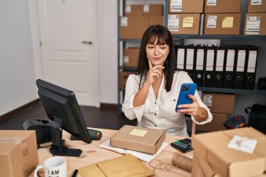 Küçük bir iş yerinde çalışan esmer bir kadın. Akıllı telefon kullanıyor. Ciddi bir yüz ifadesi takınıyor. 