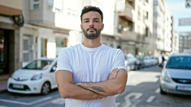 Ciddi bir ifadeyle ve kollarını kavuşturarak sokakta dikilen İspanyol genç bir adam.