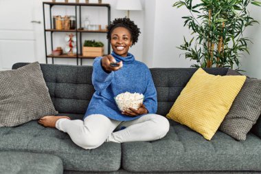 Afro-Amerikalı kadın evde kanepede oturmuş film izliyor.