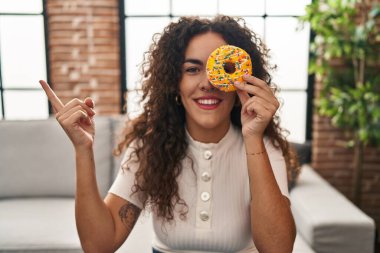 Lezzetli bir donut gözü tutan genç İspanyol kadın gülümsüyor mutlu bir şekilde eli ve parmağı yana doğru işaret ediyor. 