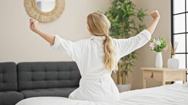 Genç sarışın kadın yatak odasında kollarını esneterek uyanıyor.