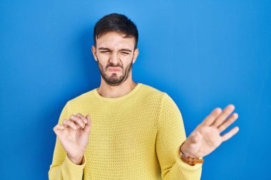 Hispanik adam mavi arka planda duruyor, tiksinti ifadesi, hoşnutsuz ve korku dolu bir yüz ifadesi çünkü tiksinti tepkisi. 