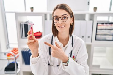 Kafkasyalı genç doktor elinde jilet tutarken mutlu bir şekilde eli ve parmağı işaret ediyor. 