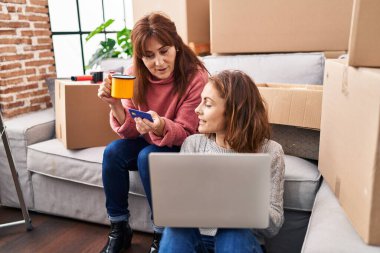 Two women mother and daughter using laptop and credit card drinking coffee at new home