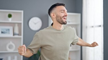 Genç İspanyol adam gülümseyerek evde dans ediyor.