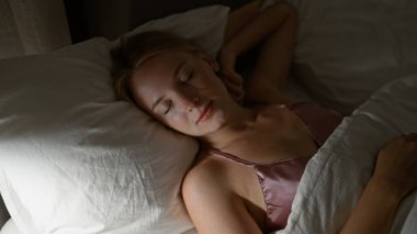 Genç sarışın kadın yatakta uzanıyor, yatak odasında uyuyor.