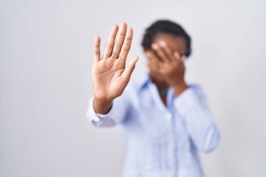 Beyaz arka plan üzerinde duran Afrikalı kadın gözlük takıyor, gözleri elleriyle örtüyor ve üzgün ve korku ifadeleriyle jestleri durduruyor. utangaç ve olumsuz kavram. 