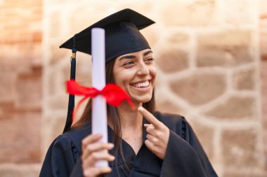 Mezuniyet üniforması giyen genç İspanyol kadın üniversiteyi parmağıyla işaret ediyor.