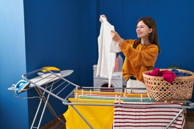 Gömleğini tutan genç sarışın kadın çamaşırhanede çamaşır ipine asıyor.