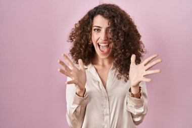 Hispanic woman with curly hair standing over pink background celebrating crazy and amazed for success with arms raised and open eyes screaming excited. winner concept 