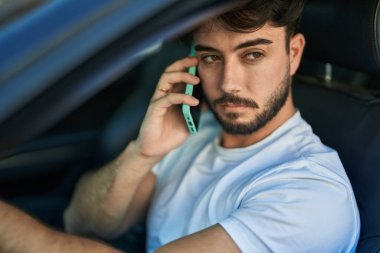 Genç İspanyol adam akıllı telefondan konuşuyor. Sokakta arabada oturuyor.