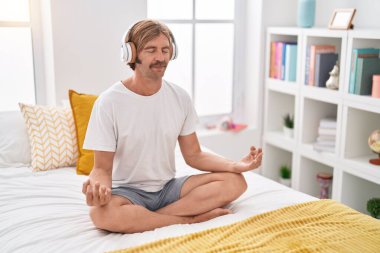 Young blond man doing yoga exercise sitting on bed at bedroom