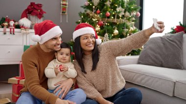 Çift ve oğul akıllı telefondan özçekim yapıyorlar. Evdeki Noel ağacının yanında oturuyorlar.