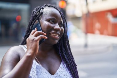 Afro-Amerikalı kadın gülümsüyor. Akıllı telefondan konuşuyor.