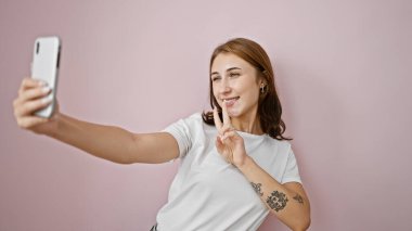 Genç bir kadın kendine güveni tam. Akıllı telefonun yanında özçekim yapıyor. Pembe arka planda.