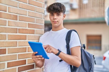 Young hispanic teenager student using touchpad with relaxed expression at street