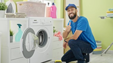 Genç İspanyol teknisyen alet çantası tutuyor. Çamaşır odasında el hareketi yapıyor.