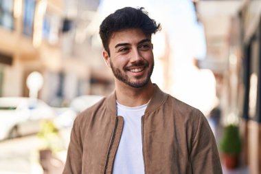 Young hispanic man smiling confident looking to the side at street
