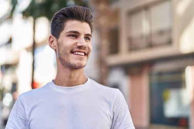Young hispanic man smiling confident looking to the side at street