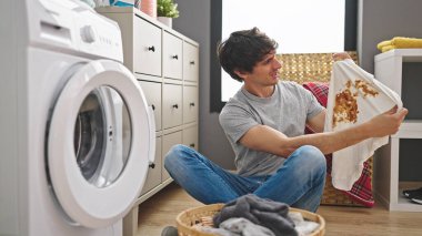 Çamaşır odasında kirli tişört tutan İspanyol bir adam çamaşır yıkıyor.