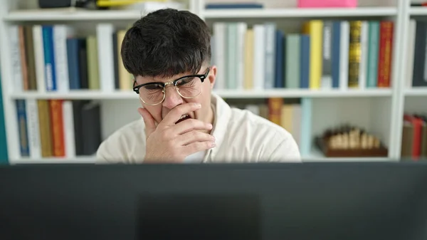 Young hispanic man student tired using computer yawning at library university