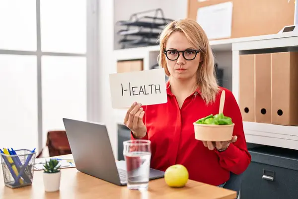 在办公室工作的金发女人吃着健康的食物 她怀疑和紧张 因为问题而皱着眉头 消极的人 — 图库照片
