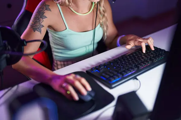 Young blonde woman using computer keyboard and mouse at gaming room