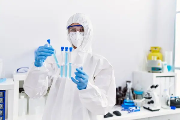 Young blonde woman scientist wearing security uniform holding test tubes at laboratory