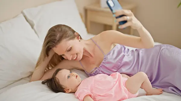 Mother and daughter lying on bed make selfie by smartphone kissing at bedroom