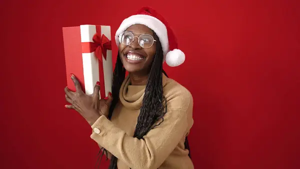 Afrikaanse Vrouw Glimlachen Zelfverzekerd Holding Kerstcadeau Geïsoleerde Rode Achtergrond — Stockfoto