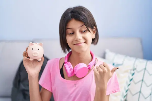 Jovem Menina Segurando Porquinho Banco Apontando Polegar Até Lado Sorrindo — Fotografia de Stock