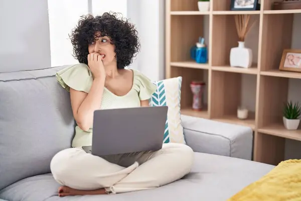 若いブルネットの女性は 自宅でソファーに座っているラップトップを使用して ストレスを感じて 爪を噛む手で緊張しています 不安問題 — ストック写真