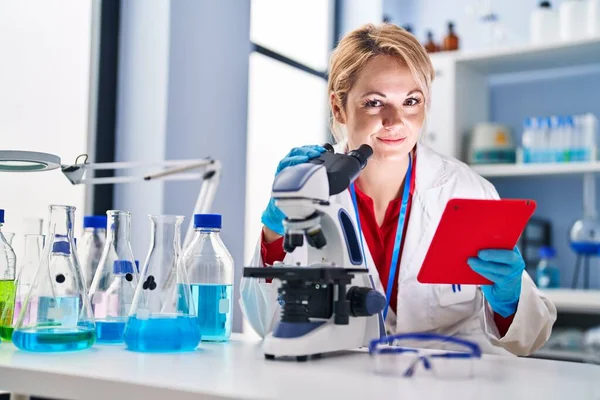 Laboratuvarda dokunmatik ped ve mikroskop kullanan genç sarışın kadın bilim adamı.