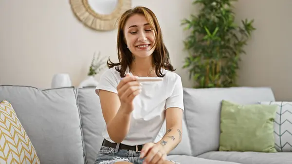 自宅で祝う妊娠テストを開催するソファに座っている若い女性 — ストック写真