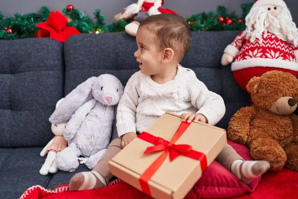 家でソファーに座っているクリスマスの贈り物を荷を下ろす愛らしいヒスパニックの幼児 — ストック写真