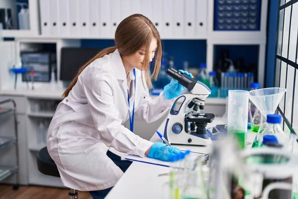 stock image Young caucasian woman scientist using microscope write on document at laboratory