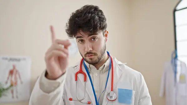Young hispanic man doctor saying no with finger at clinic