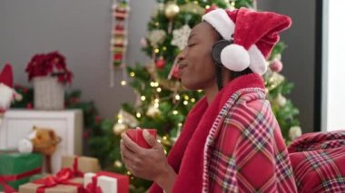 Afrika kökenli Amerikalı bir kadın müzik dinliyor. Kahve içiyor. Yılbaşı ağacının yanında oturuyor.