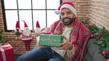 Noel hediyesini elinde tutan İspanyol genç adam evdeki kanepede oturuyor.