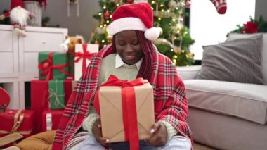 Saçları örgülü, elinde Noel hediyesi olan Afrikalı bir kadın evde yerde oturuyor.