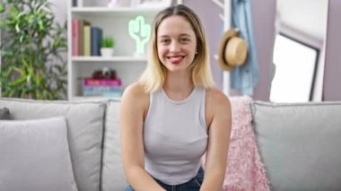 Kanepede oturan genç sarışın kadın baş parmak hareketi yapıyor ve evdeki kafasıyla evet diyor.