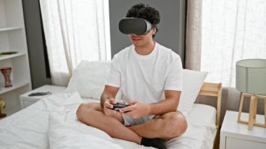 Sanal gerçeklik gözlüğü ve joystick kullanarak video oyunu oynayan genç latin adam yatak odasında kutlama yapıyor.