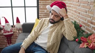 Kanepede uyuyan İspanyol genç adam evde Noel şapkası takıyor.