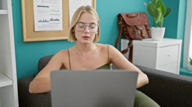 Genç sarışın iş kadını. Laptop kullanıyor. Ofise bakıyor.