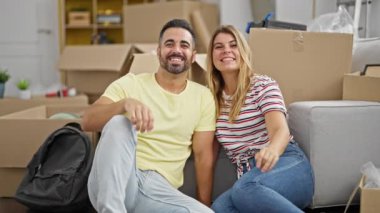 Erkek ve kadın çiftin yeni evlerinde yerde otururken videoları var.