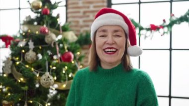 Evde Noel ağacının yanında gülümseyen gri saçlı olgun İspanyol kadın.