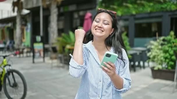 年轻的中国女人在咖啡店的阳台上用智能手机庆祝 — 图库视频影像
